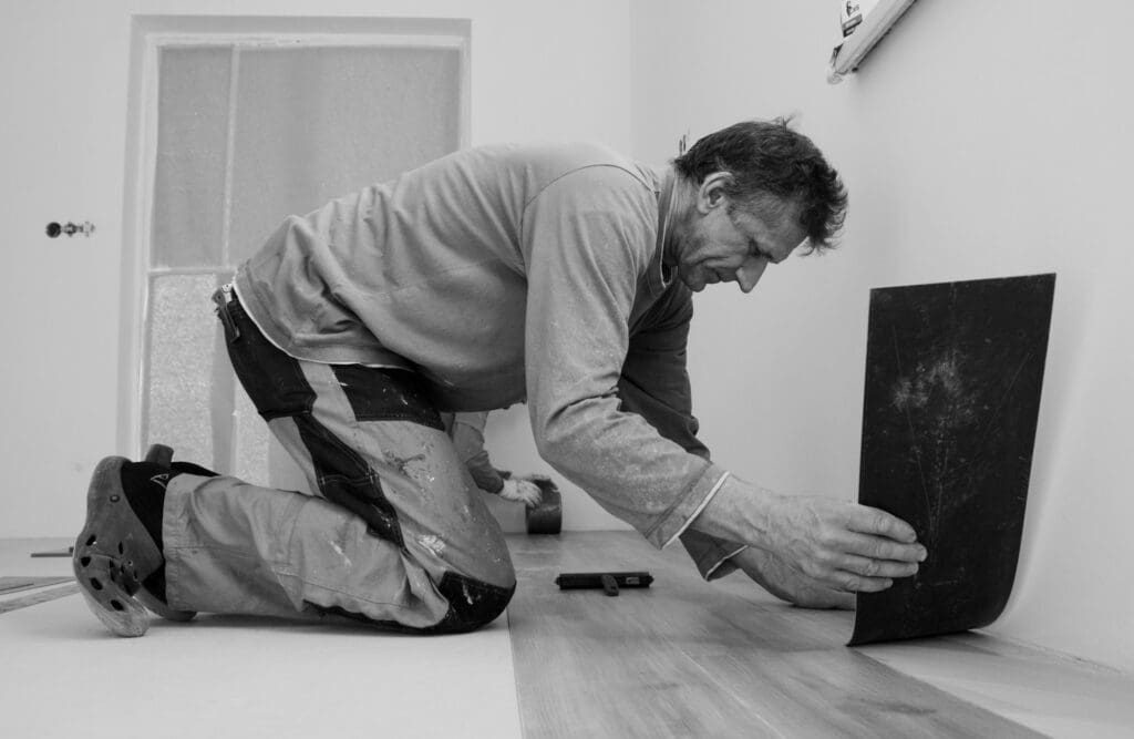 A person lifting worn vinyl floor tiles during a home renovation project