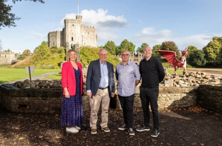 Four people standing in front of a castle keep beside a red dragon sculpture
